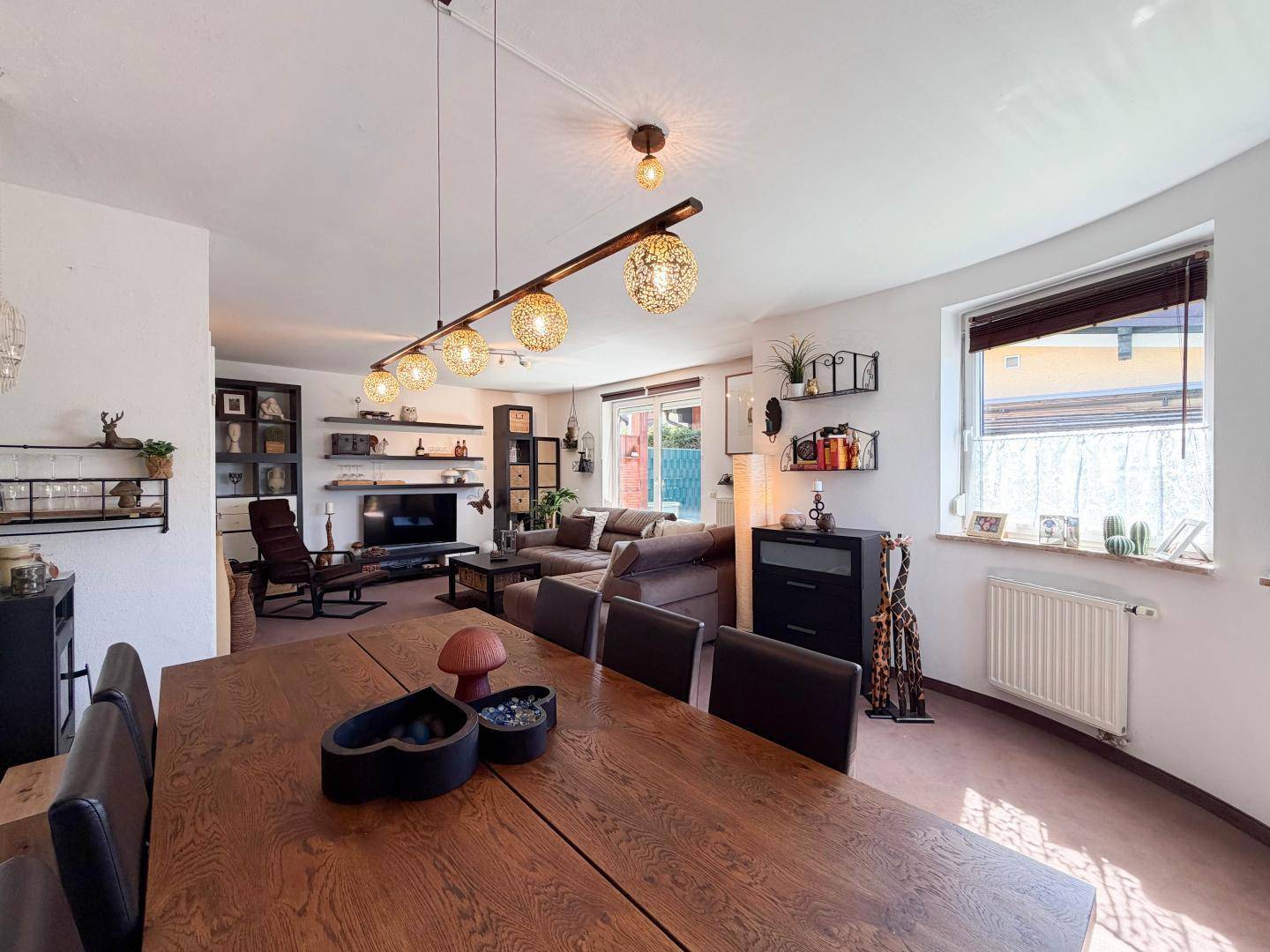 Geräumiger Wohn- und Essbereich mit großem Holztisch, bequemer Couch und Blick in den Garten.
