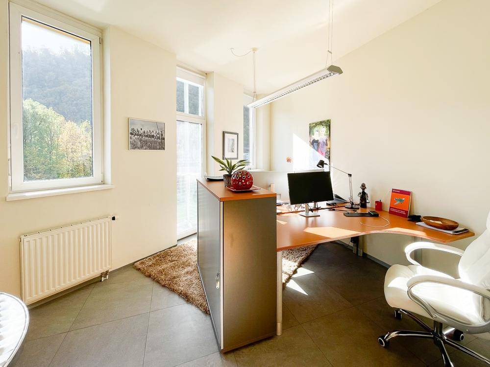 Geräumiges Büro mit geschwungenem Schreibtisch, Bürostuhl und Zugang zu einem Balkon mit Bergblick.
