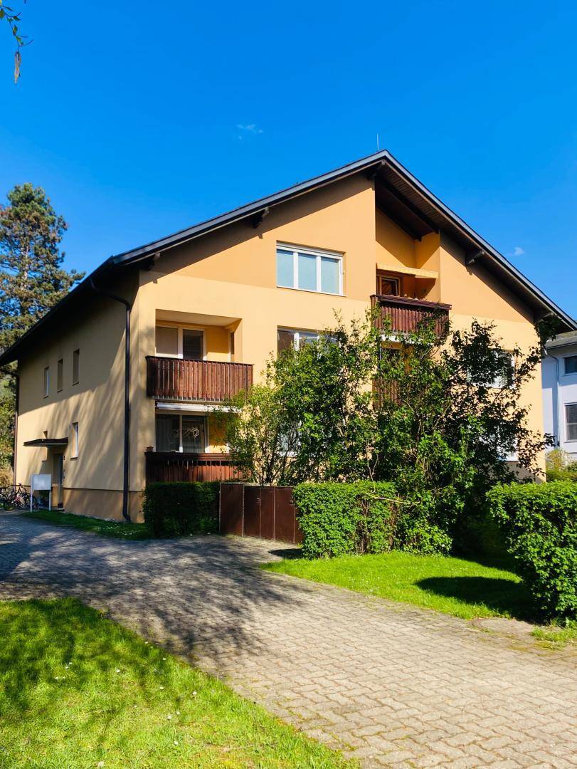 Wohngebäude mit mehreren Balkonen, umgeben von grünen Hecken und einem gepflasterten Zugang.