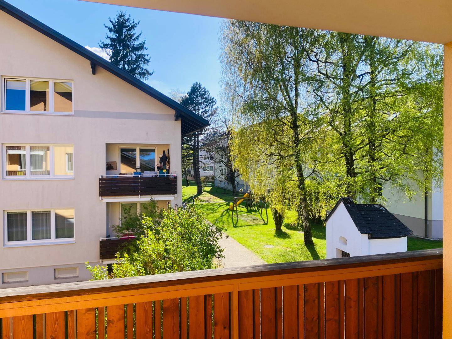 Blick vom Balkon auf die grüne Außenanlage mit Spielplatz und weiteren Wohngebäuden.