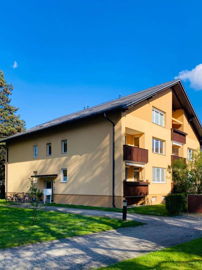 Seitenansicht eines Wohnhauses mit Balkonen, gepflegter Fassade und grünem Vorgarten.