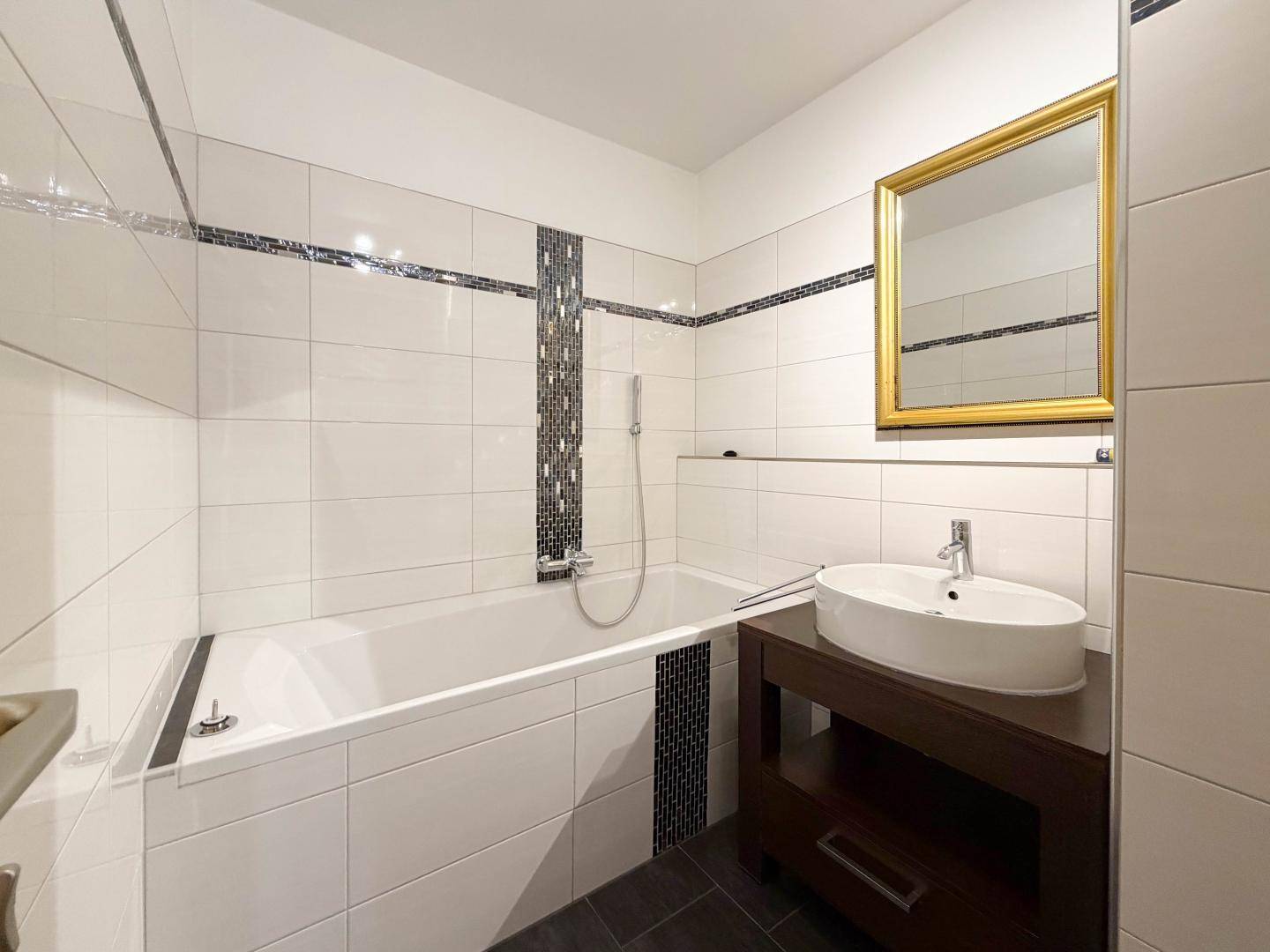 Modernes Badezimmer mit Badewanne, Waschtisch und eleganten Fliesen in Weiß und Schwarz.