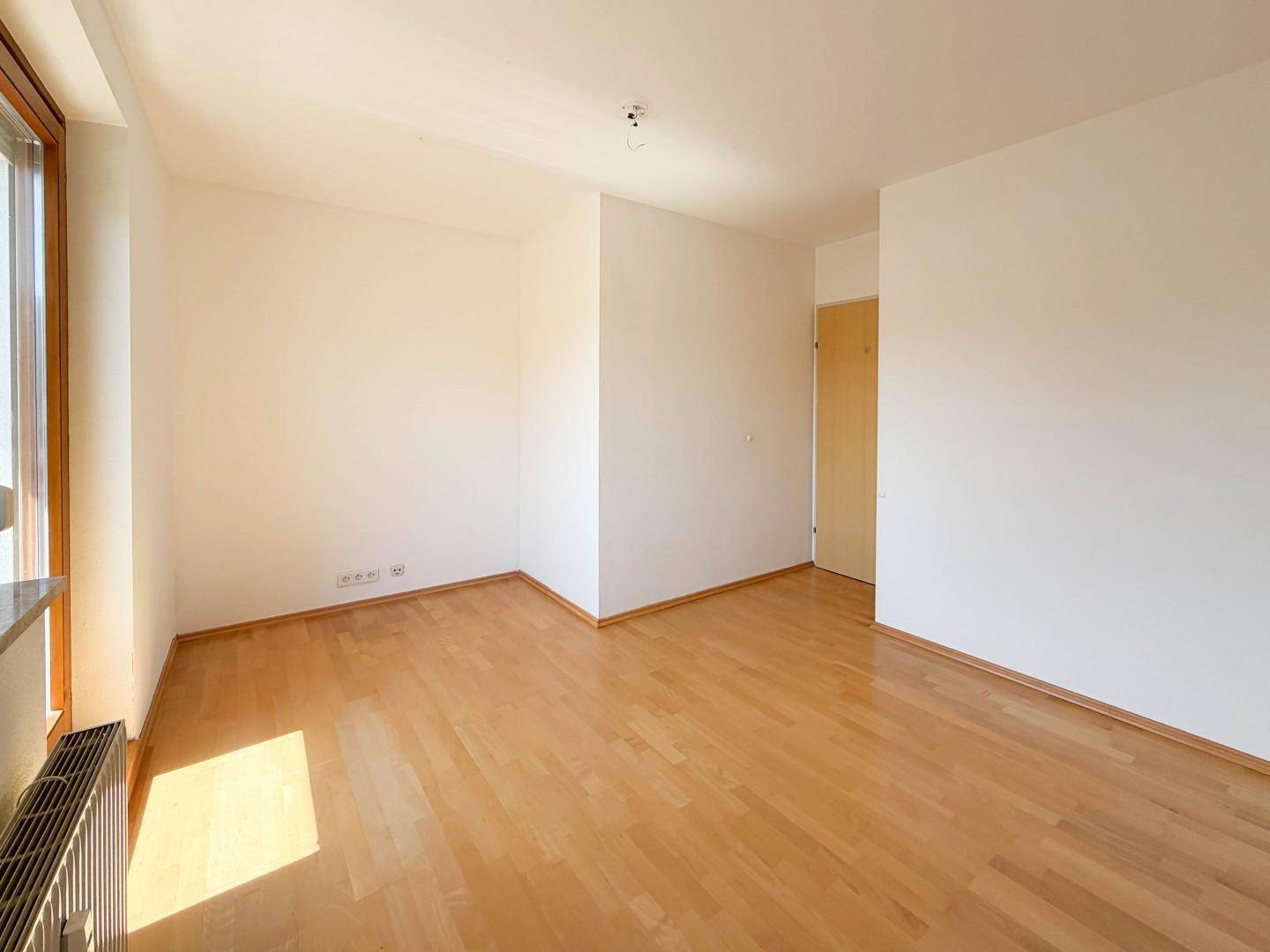 Heller Raum mit großen Fenstern, Parkettboden und viel Tageslicht.