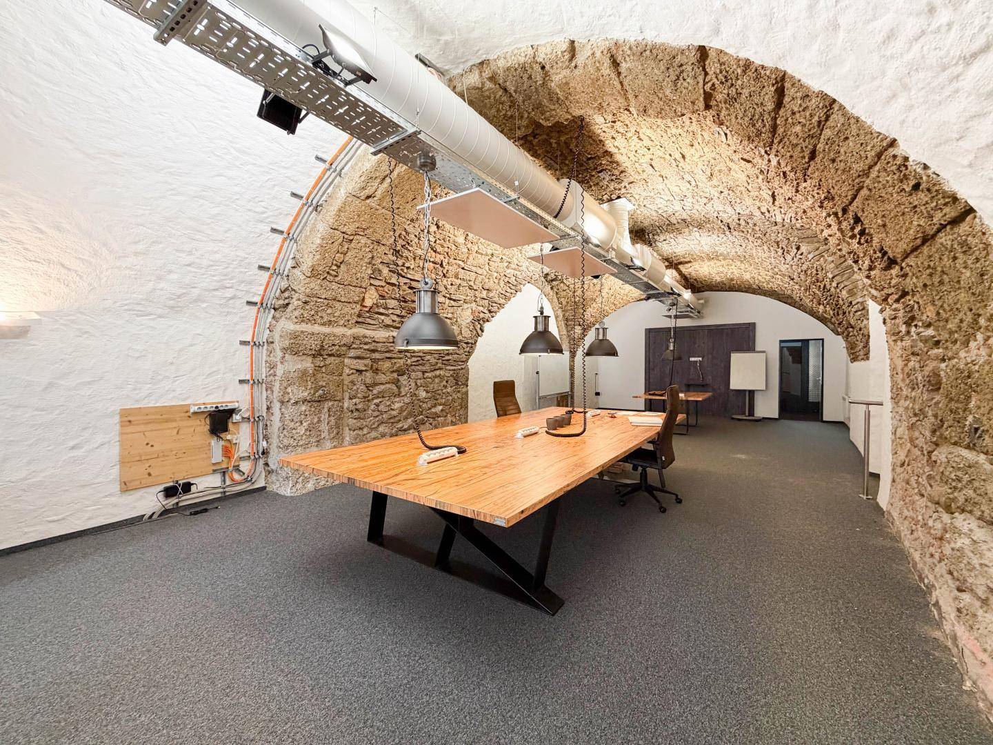 Moderner Arbeitsbereich mit Holztischen und ergonomischen Stühlen unter den beeindruckenden Steinbögen des Kellers.