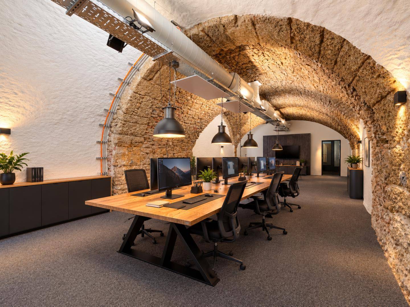 Modernes Büro in einem historischen Gebäude mit Gewölbedecken und gut ausgestatteten Arbeitsbereichen.