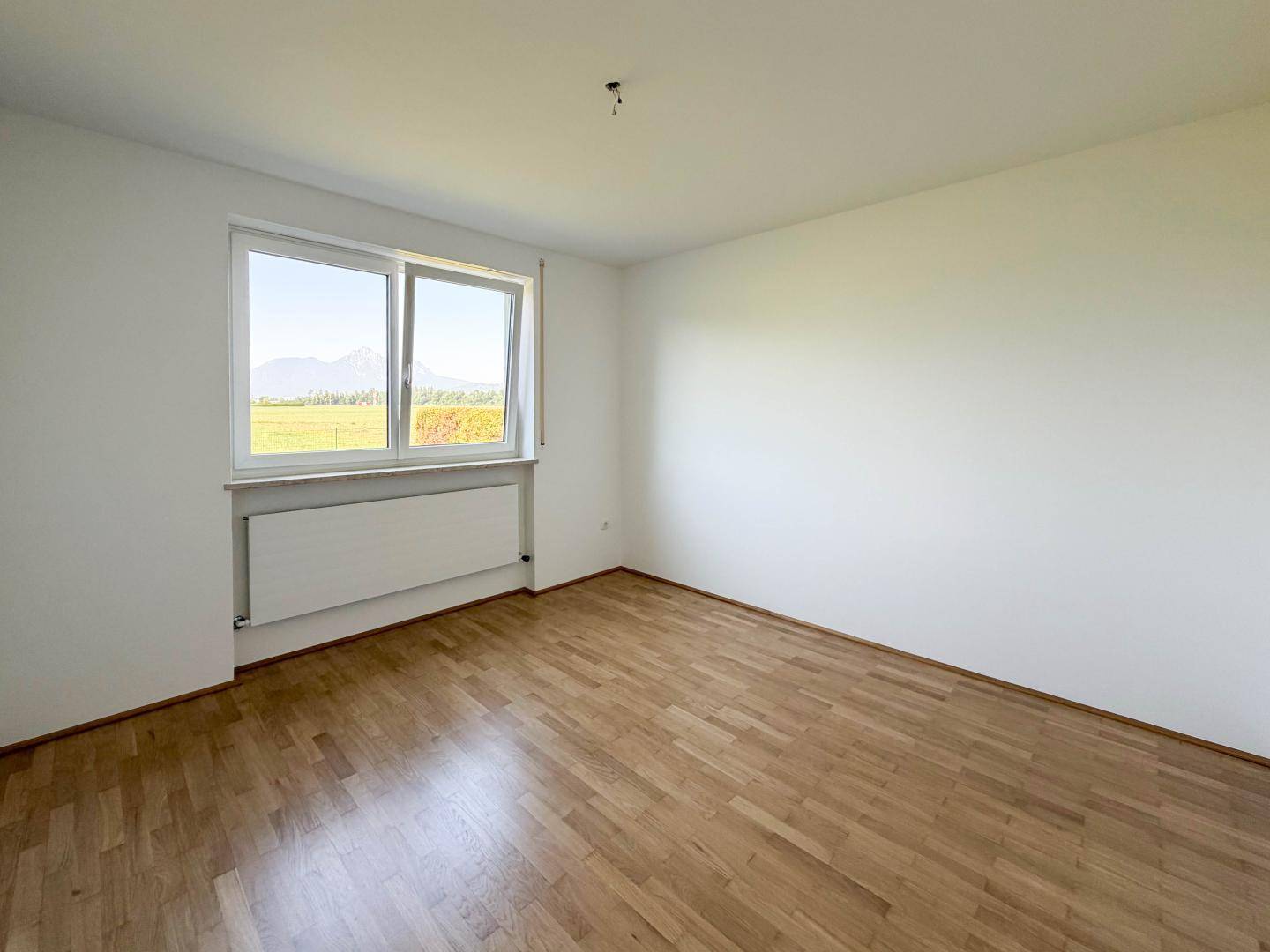 Geräumiges Zimmer mit Parkettboden und Fenster, das einen schönen Blick auf die Berge bietet.