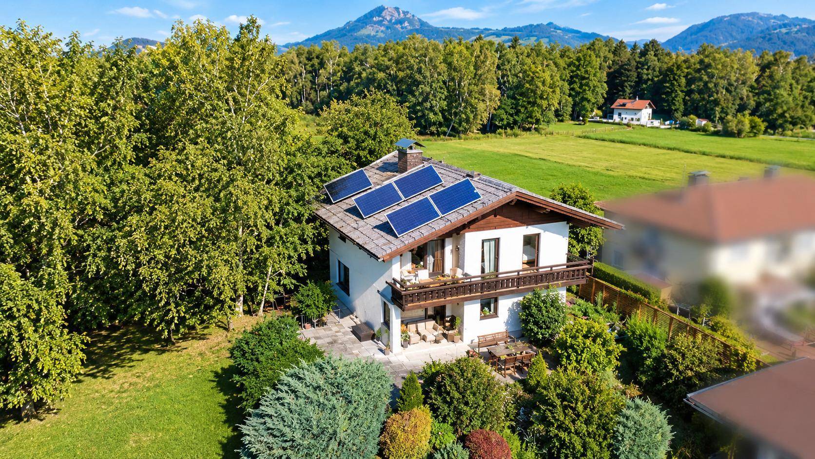Haus mit Solaranlage in ländlicher Umgebung, umgeben von Bäumen und mit Bergblick.