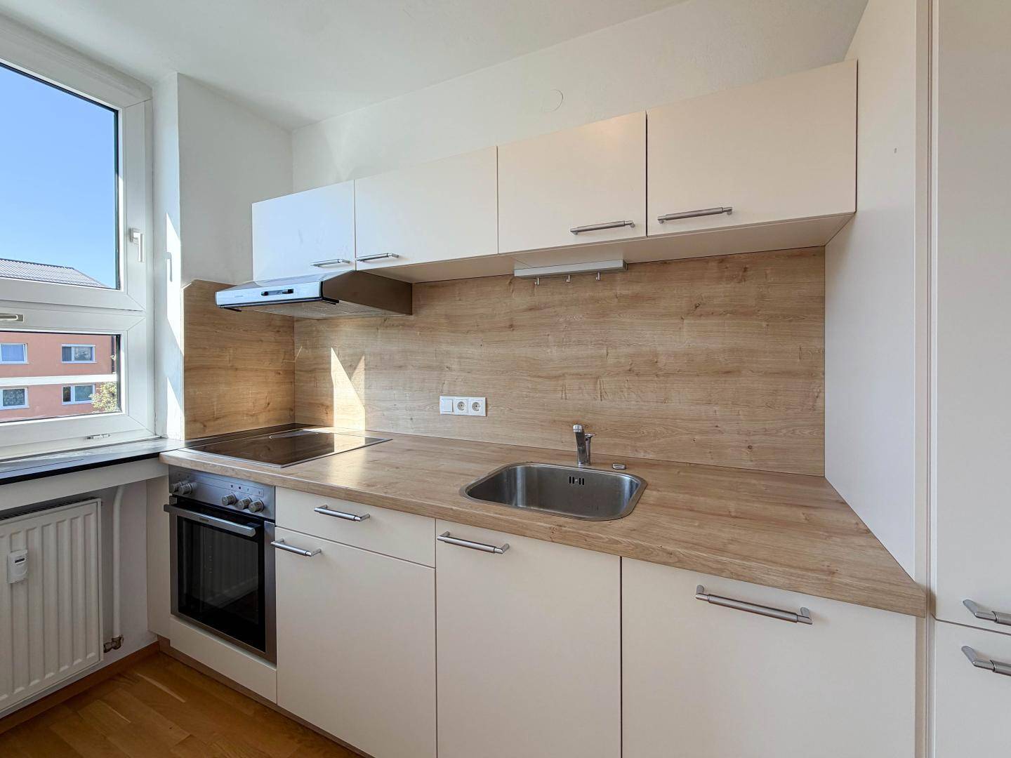 Kompakte Einbauküche mit hellem Holzdekor, weißen Schränken und Fenster für Tageslicht.