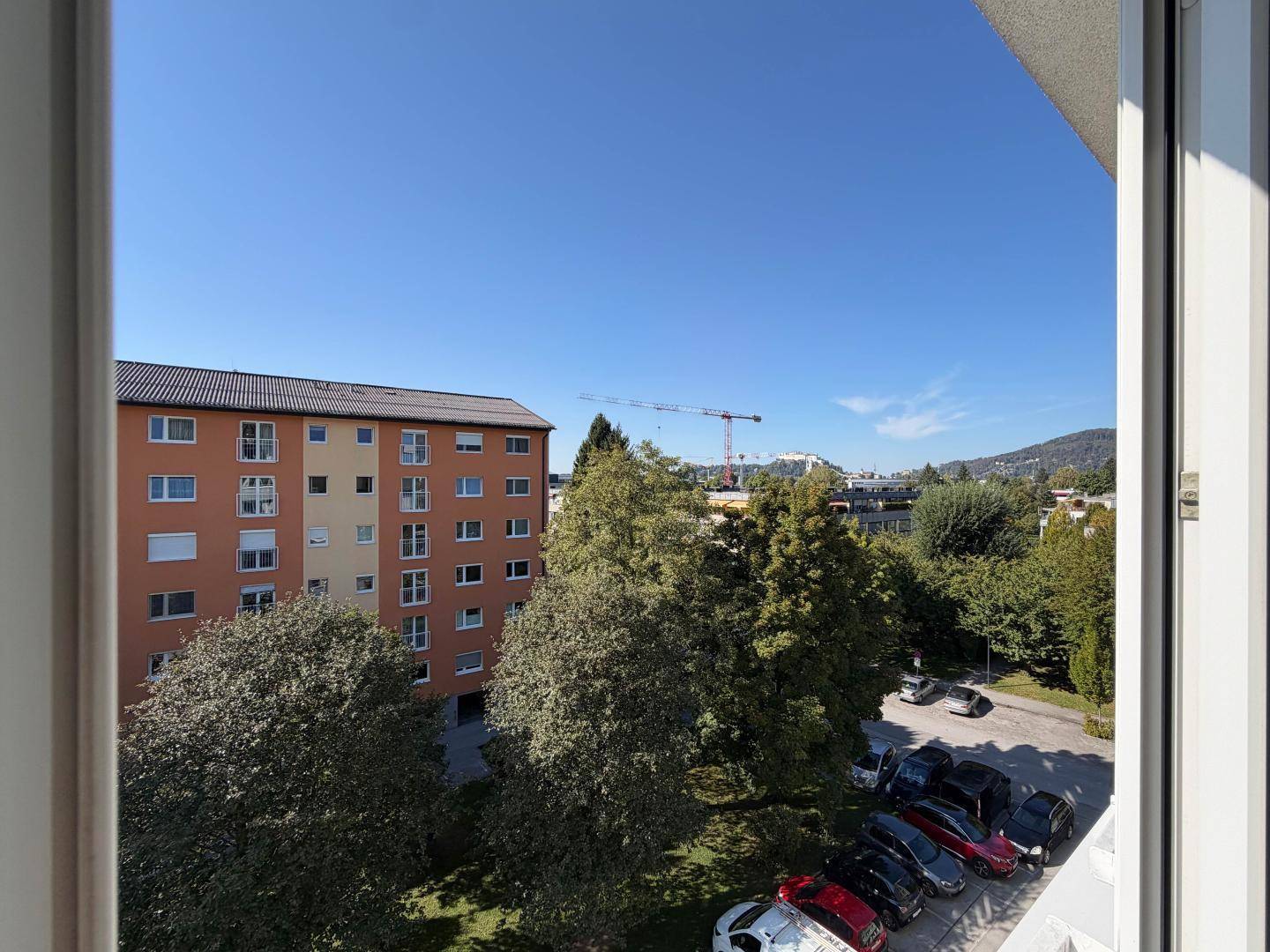 Ausblick aus dem Fenster auf umliegende Wohngebäude, Bäume und einen Parkplatz.