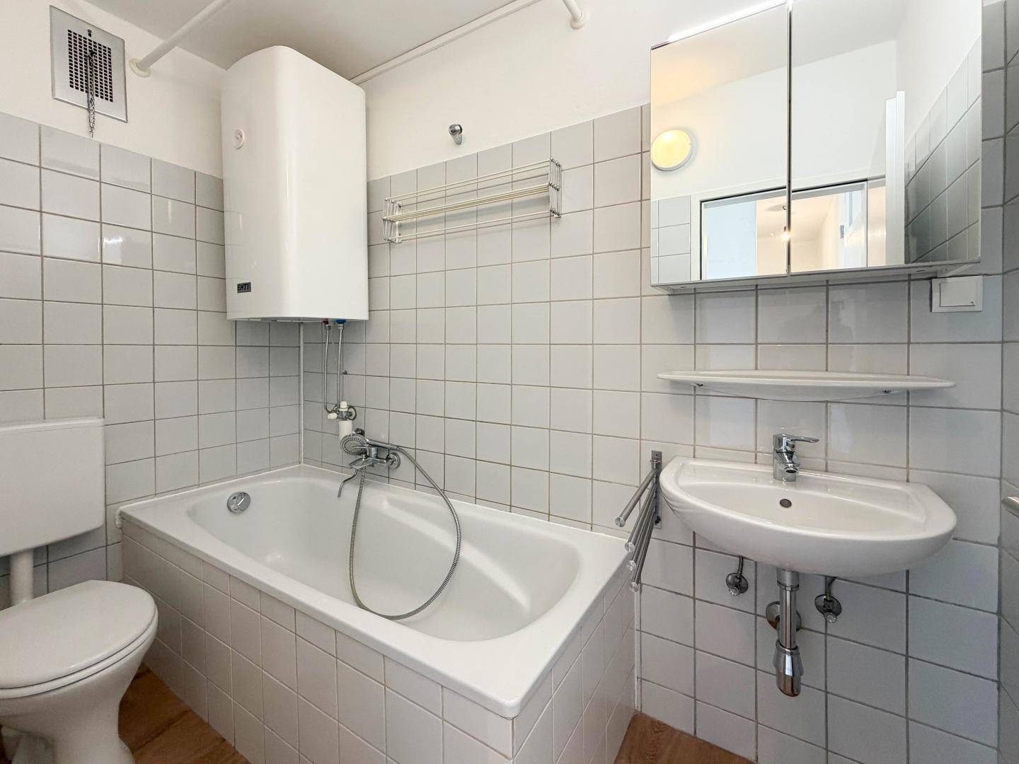 Funktionales Badezimmer mit Badewanne, Waschbecken, Spiegelschrank und weißen Wandfliesen.
