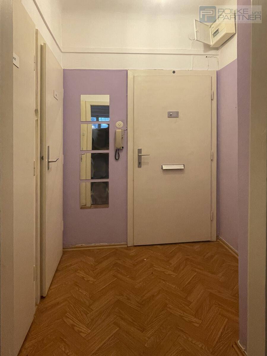 Eingangsbereich mit Fischgrätparkett, lila Wänden und einer großen Wohnungstür.