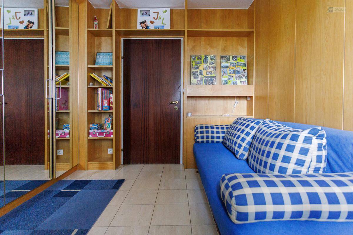 Schlafzimmer mit blauer Couch, Holzvertäfelung und integrierten Regalen und Schränken.