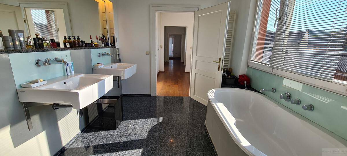 Modernes Badezimmer mit Doppelwaschbecken, Badewanne und Fenster mit Jalousien.