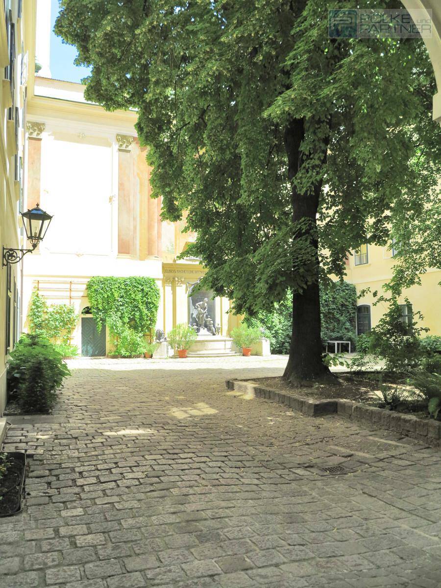 Historischer Innenhof mit Kopfsteinpflaster, altem Baum und klassischer Architektur.