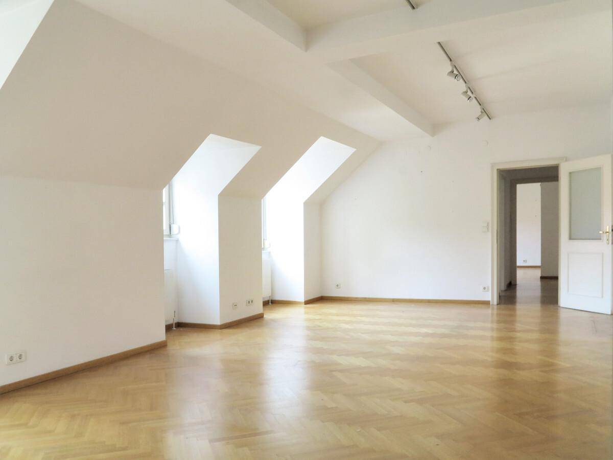 Geräumiges Wohnzimmer mit Fischgrätparkett, Dachschrägen und viel Tageslicht.
