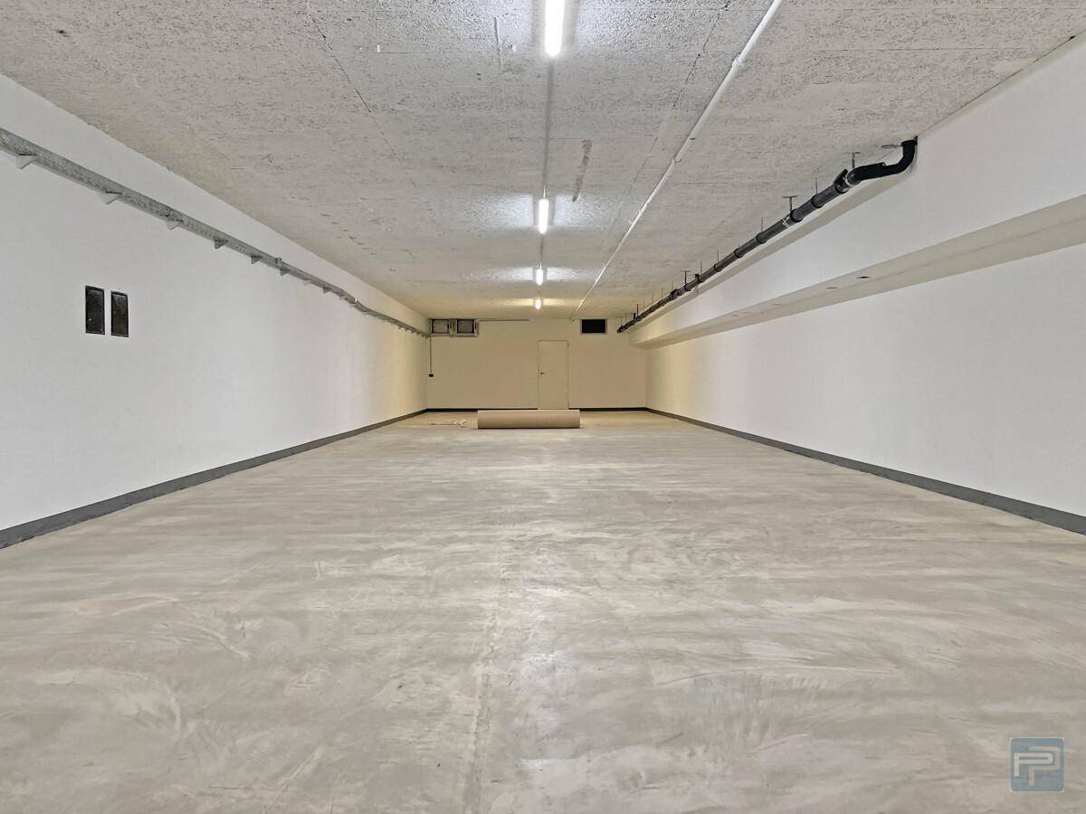 Geräumiger Kellerraum mit Sichtbetonboden, weißen Wänden und sichtbaren Installationen an der Decke.
