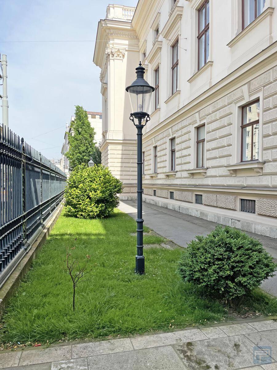 Seitenansicht eines historischen Gebäudes mit schmiedeeisernem Zaun, Rasenfläche und klassischer Straßenlaterne.