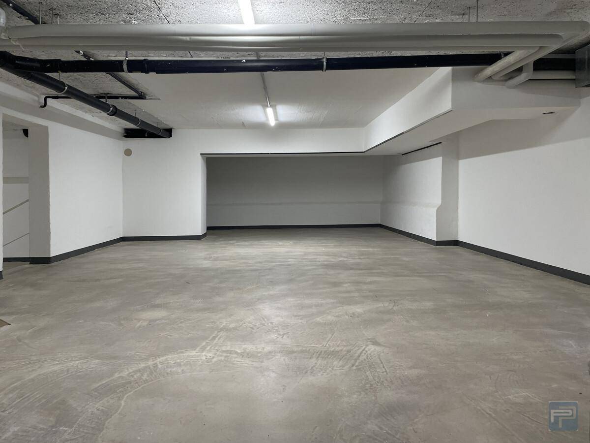 Geräumiger Kellerraum mit Sichtbetonboden, weißen Wänden und sichtbaren Installationen an der Decke.