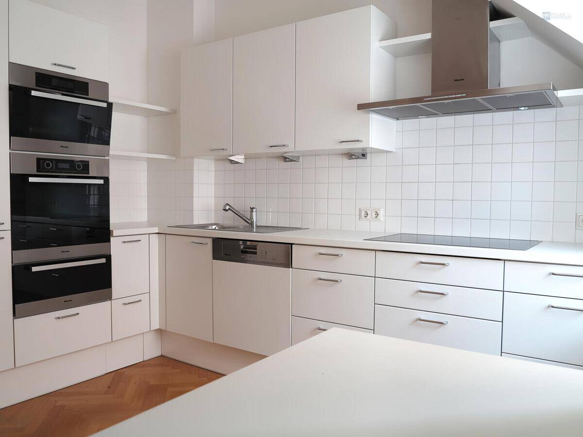 Moderne weiße Einbauküche mit integrierten Geräten, Backöfen und Induktionskochfeld.