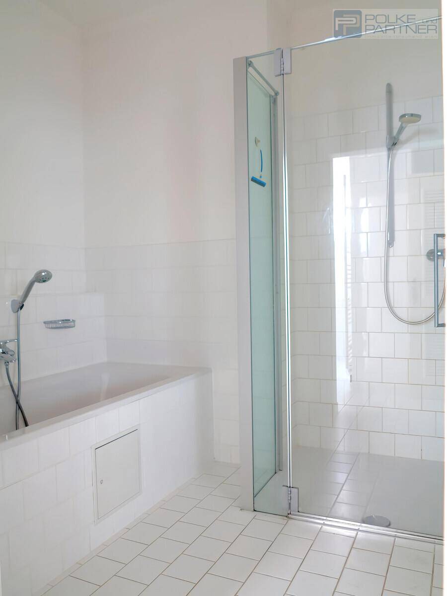 Helles Badezimmer mit weiß gefliesten Wänden, Badewanne und separater Duschkabine.