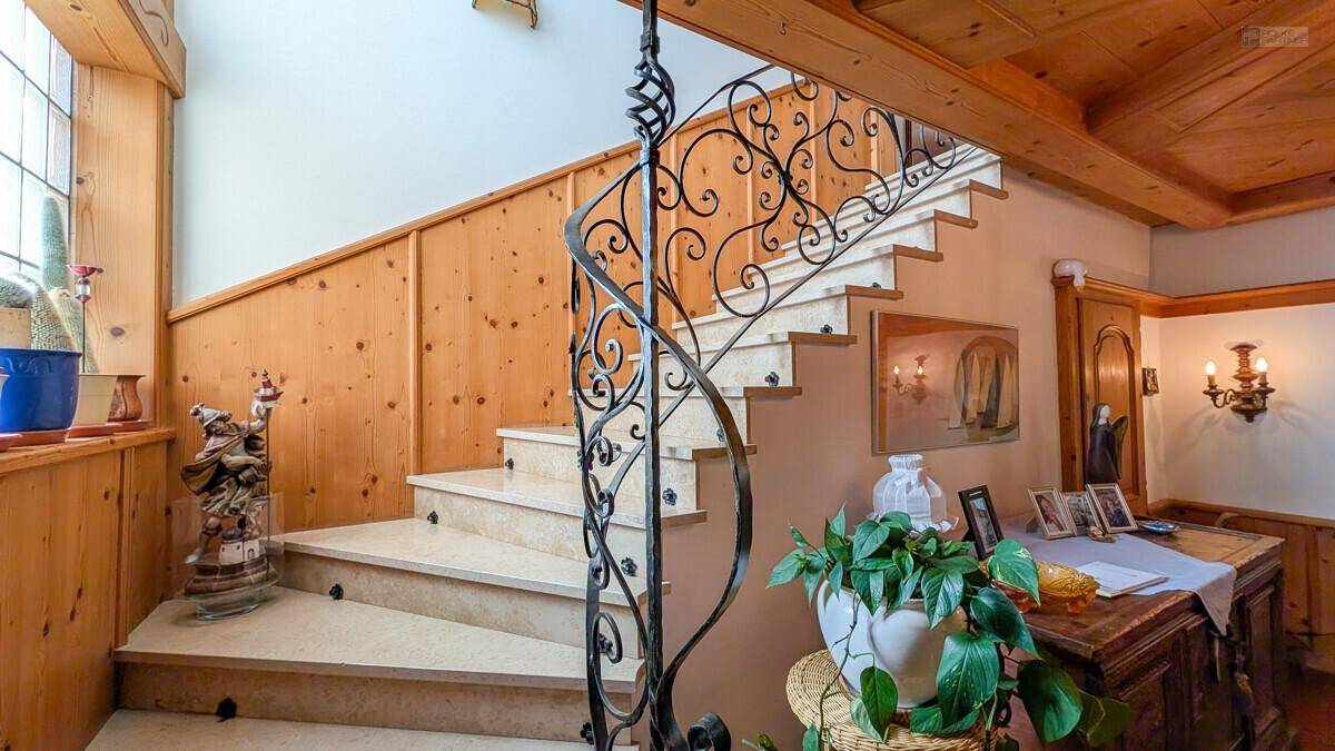 Elegante Treppe mit schmiedeeisernem Geländer und Holzvertäfelung in einem hellen Flur.
