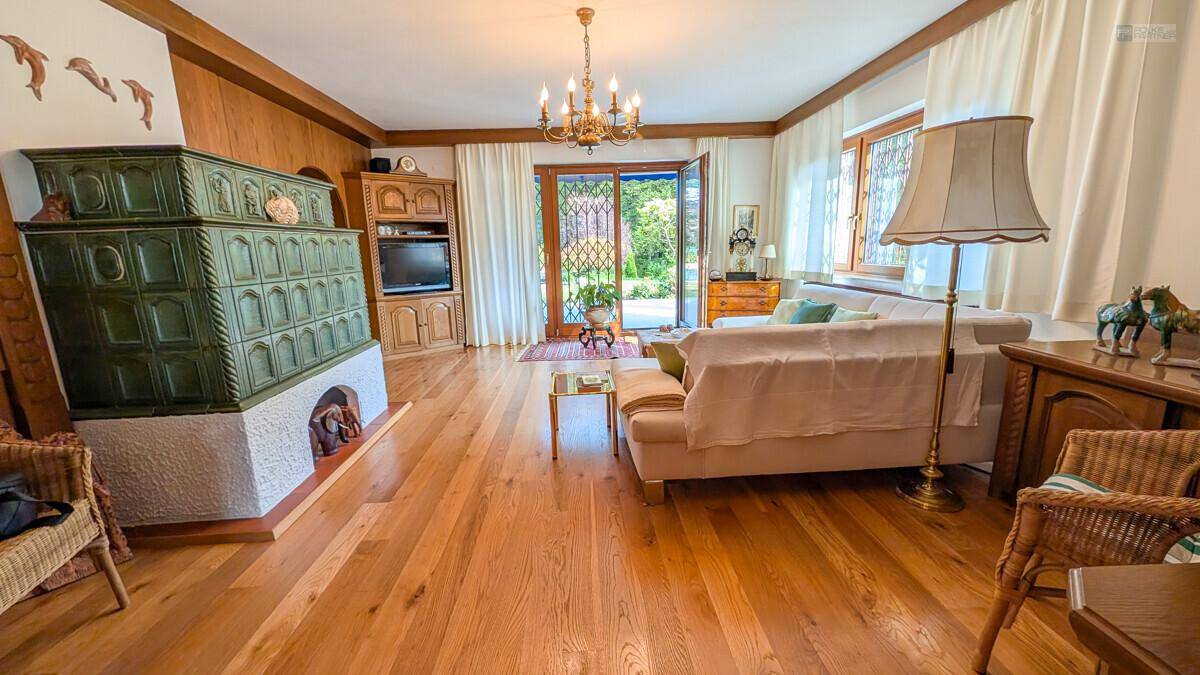 Helles Wohnzimmer mit Holzboden, traditionellem Kachelofen und Zugang zum Garten.