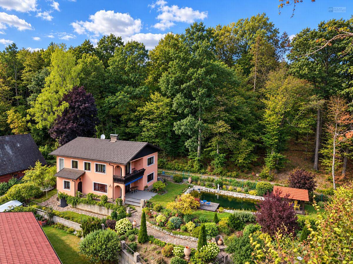Luftaufnahme eines Hauses mit weitläufigem Garten, Teich und umgebendem Wald.