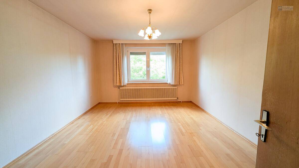 Helles Zimmer mit hellem Parkettboden und großem Fenster, bereit zur individuellen Gestaltung.