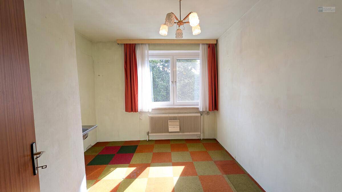 Zimmer mit farbenfrohem Teppichboden und Fenster, das viel Tageslicht hereinlässt.