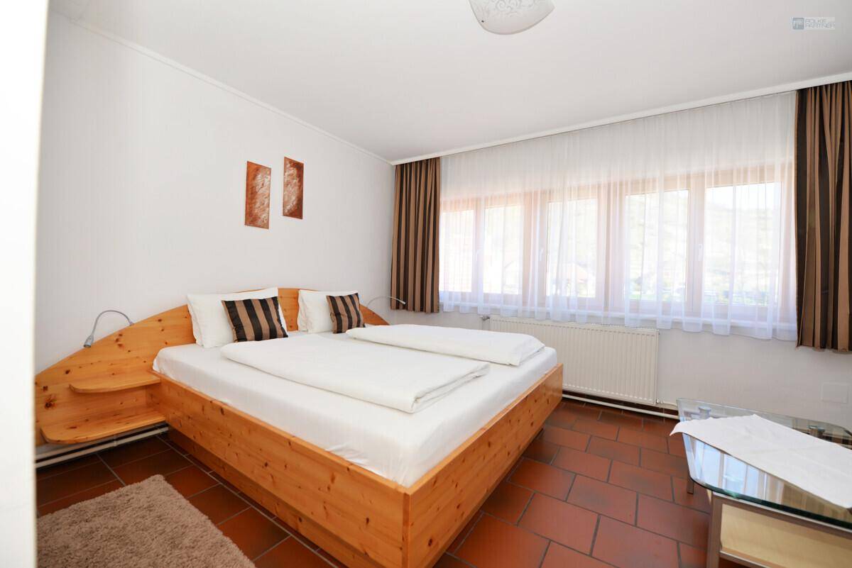 Helles Schlafzimmer mit Holzdoppelbett, Terrakotta-Fliesenboden und großen Fenstern mit Vorhängen.