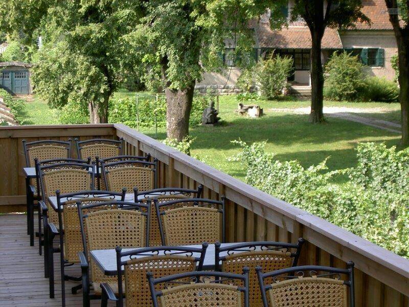 Gemütliche Terrasse mit vielen Tischen und Stühlen, umgeben von grünen Weinreben und Bäumen.