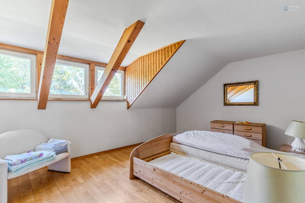 Schlafzimmer im Dachgeschoss mit Holzboden, schrägen Wänden und mehreren Fenstern.