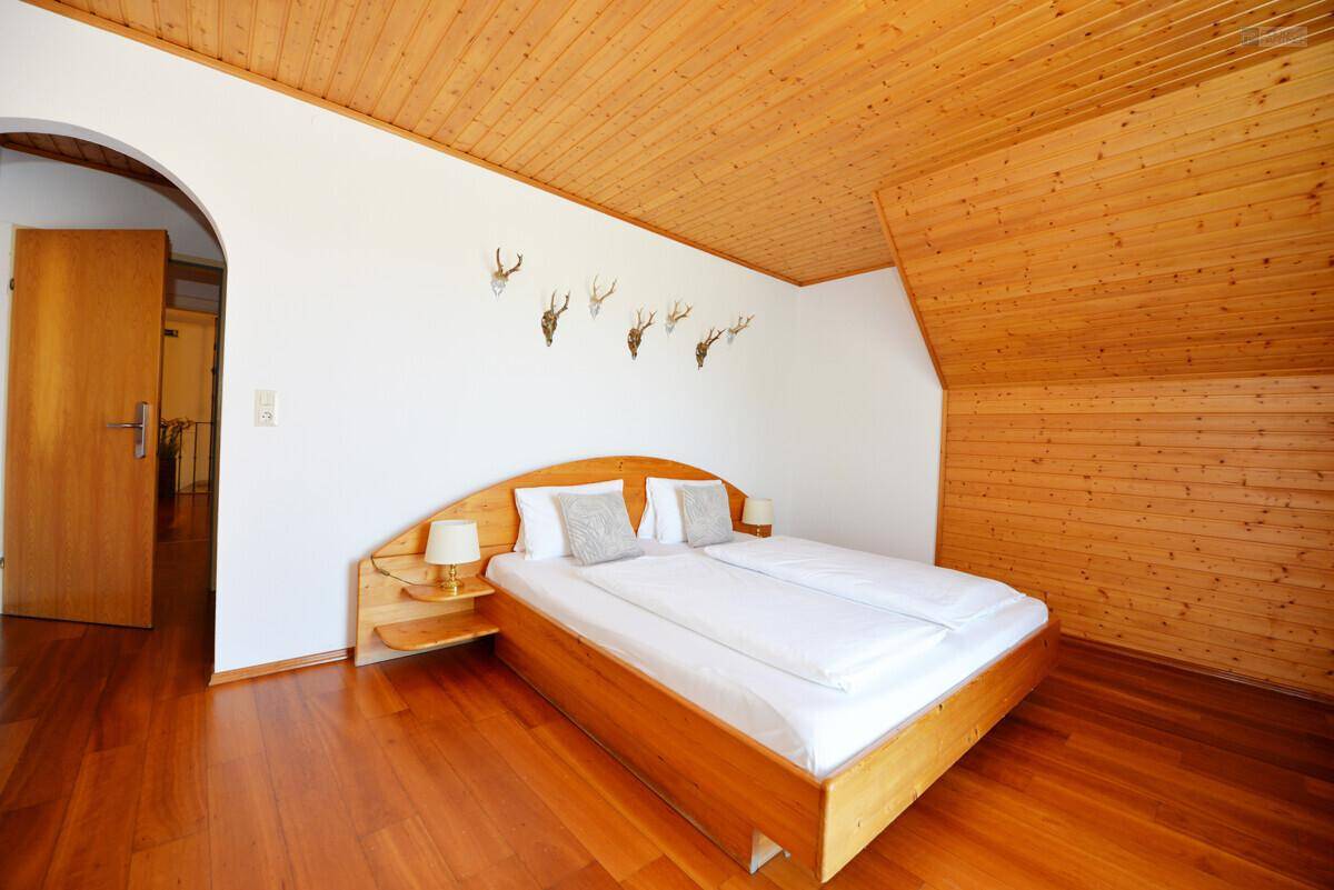 Gemütliches Schlafzimmer mit Holzdoppelbett, Holzboden und Holzdeckenverkleidung, dekoriert mit Geweihen.