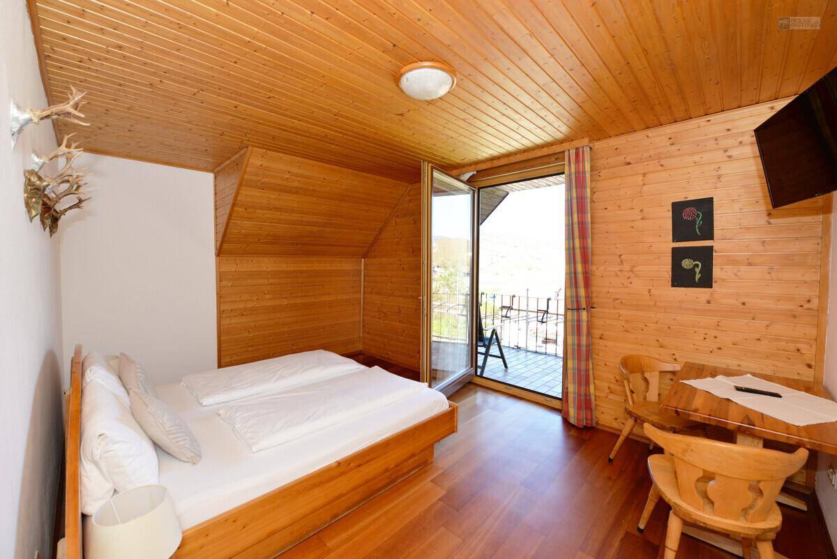 Schlafzimmer mit Holzboden, Holzdeckenverkleidung und Zugang zu einem Balkon mit Blick ins Grüne.