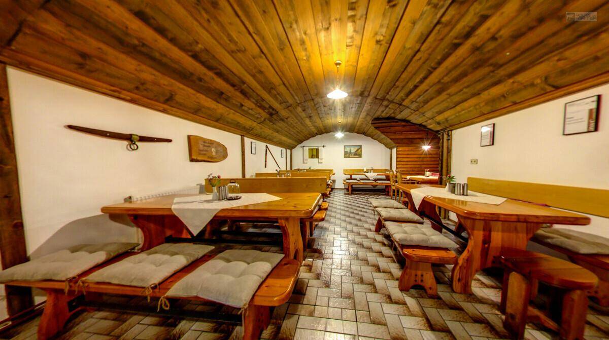 Rustikaler Speisesaal mit langen Holztischen und Bänken, Holzbalkendecke und gefliestem Boden.