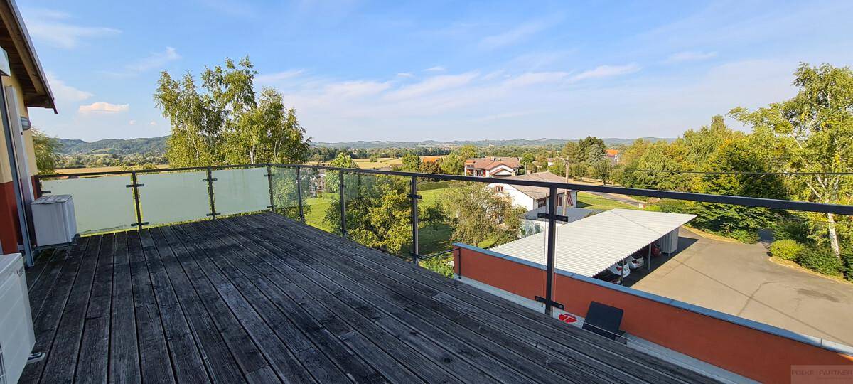 Geräumige Holzterrasse mit Glasgeländer und weitem Blick über die hügelige Landschaft.