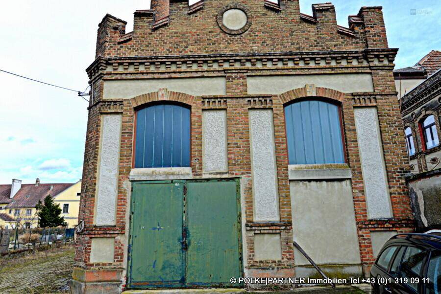 Vorderansicht eines alten Backsteingebäudes mit großen grünen Toren und Rundbogenfenstern.