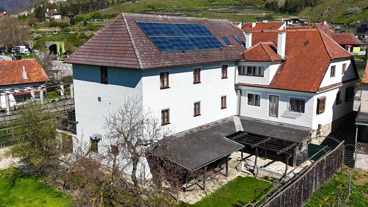 Luftaufnahme eines traditionellen Gebäudes mit Solaranlage auf dem Dach und einem gepflegten Gartenbereich.