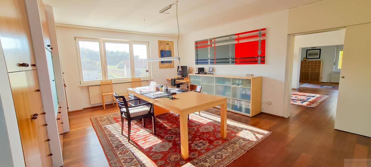 Helles Arbeitszimmer mit Holzboden, großem Schreibtisch und Blick ins Grüne.