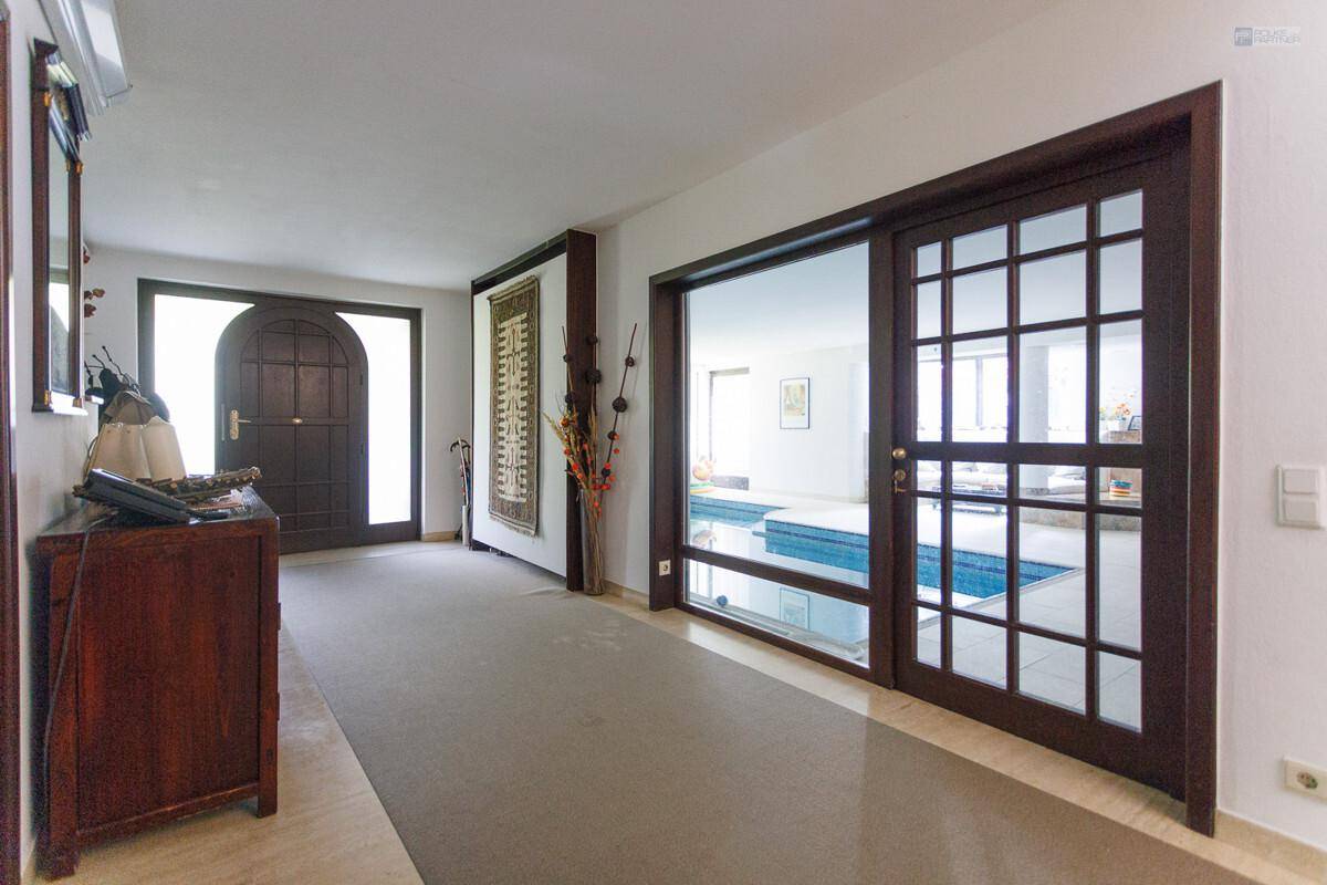 Heller Flur mit Blick durch große Fenster auf den Innenpoolbereich des Hauses.