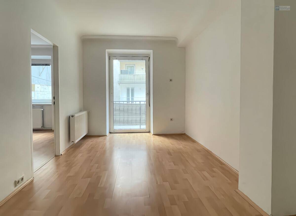 Geräumiges Zimmer mit Parkettboden und Zugang zu einem kleinen Balkon, ideal für ein Wohnzimmer.