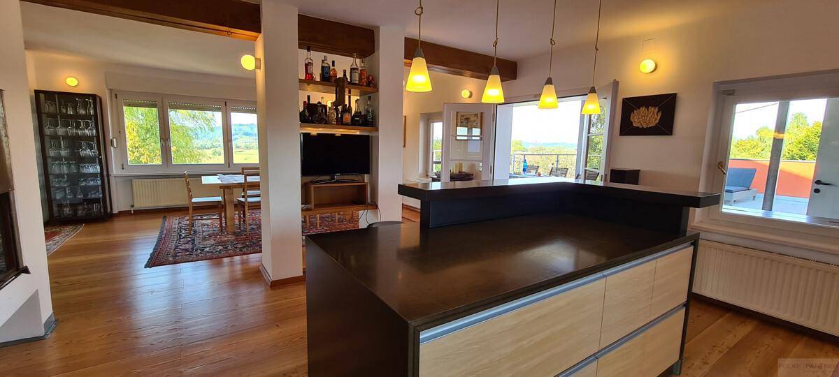 Geräumiger offener Wohnbereich mit Holzboden, Essbereich und einer Bar mit Blick ins Grüne.