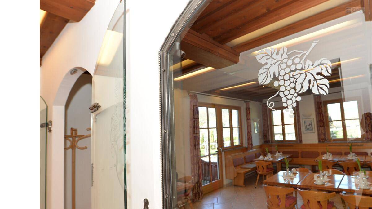 Gang mit Glaswand, die den Blick in einen traditionellen Speisesaal mit Holzbalken freigibt.