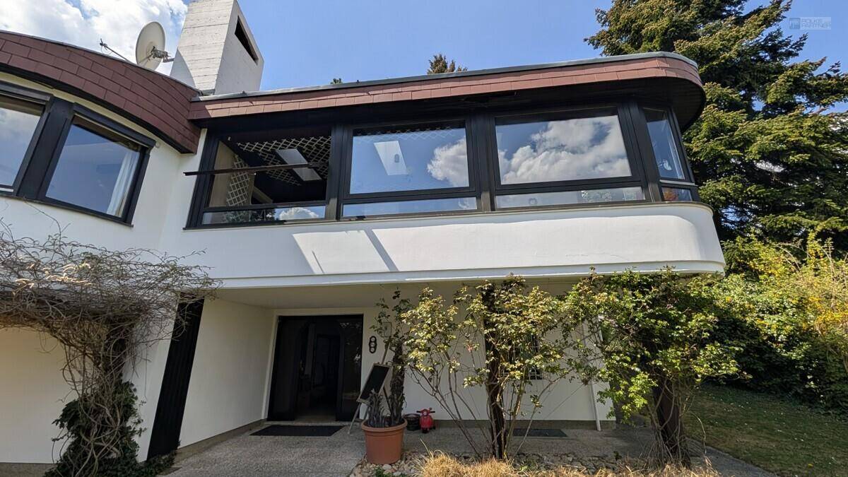 Eingangsbereich des modernen Hauses mit großen Fenstern und geschwungener Architektur.