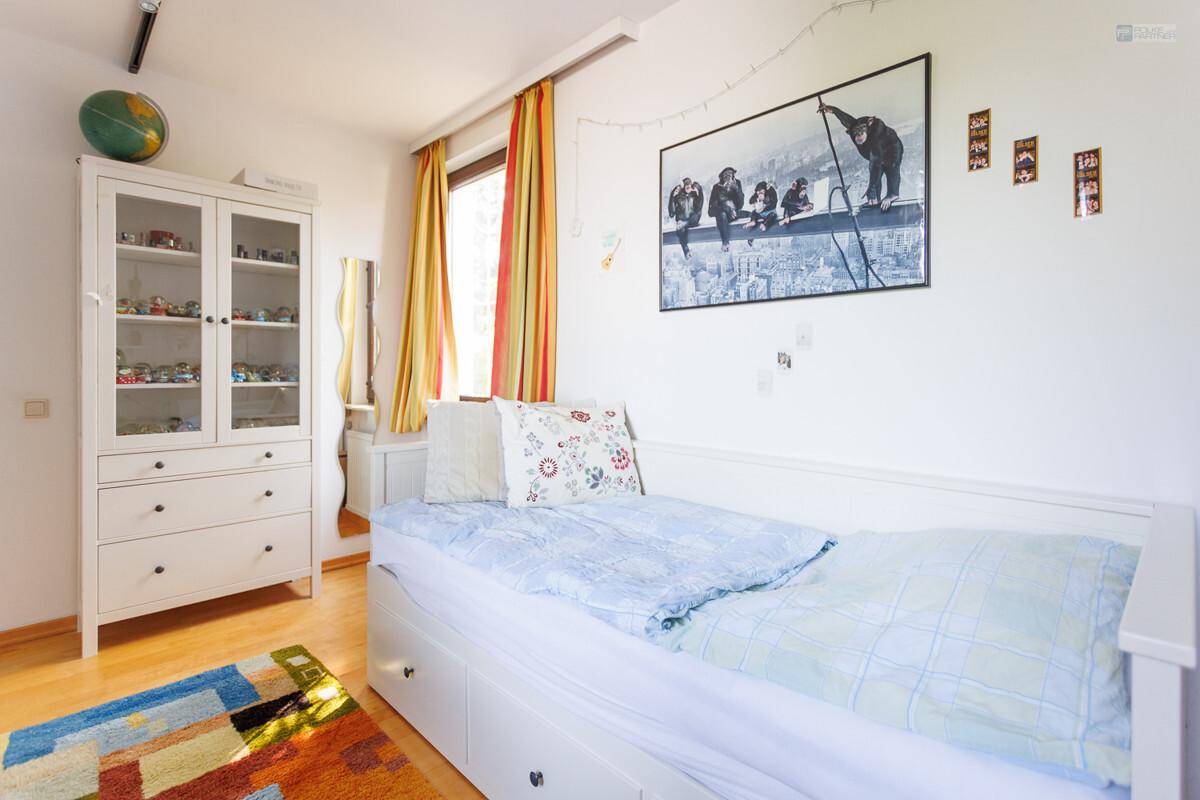 Freundliches Schlafzimmer mit Einzelbett, weißem Schrank und bunten Dekorationen.
