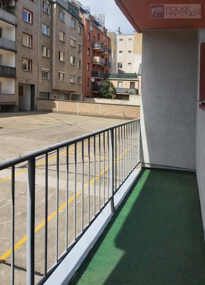 Balkon mit Kunstrasen und Blick auf einen großen Außenparkplatz sowie umliegende Wohngebäude.