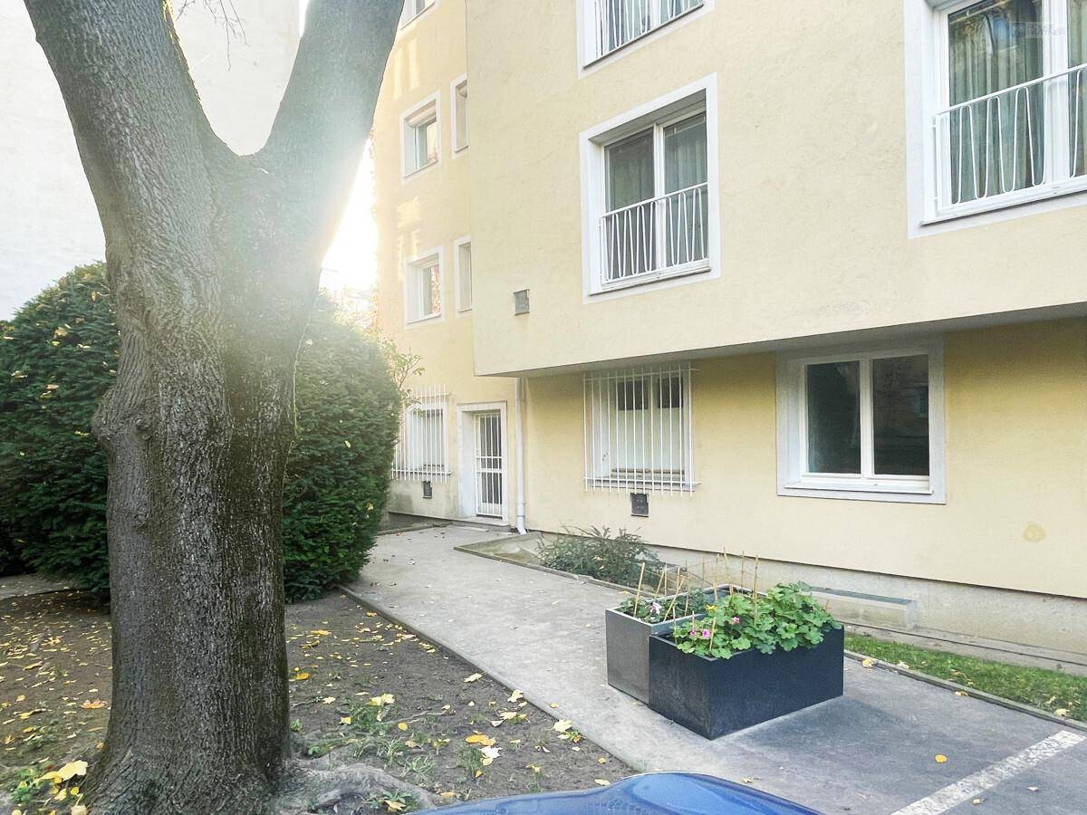 Die Fassade eines Mehrfamilienhauses mit großen Fenstern und umgebendem Grünbereich.