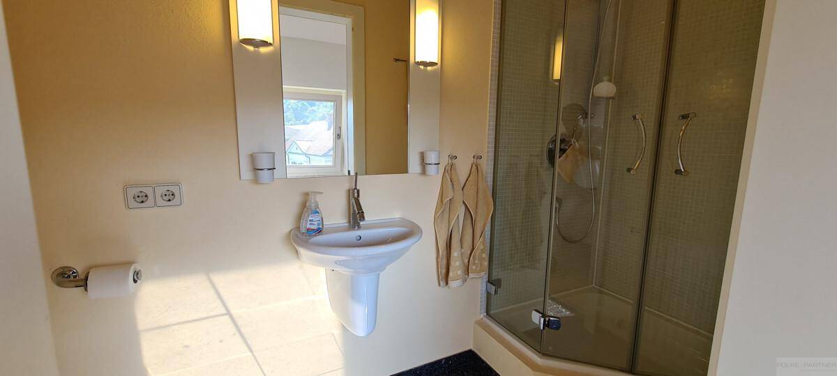 Helles Badezimmer mit Einzelwaschbecken, Spiegelschrank und Duschkabine.