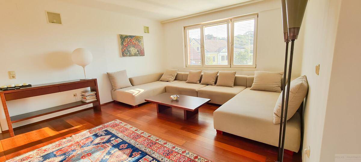 Helles Wohnzimmer mit beiger Eckcouch, Holzboden und großem Fenster.