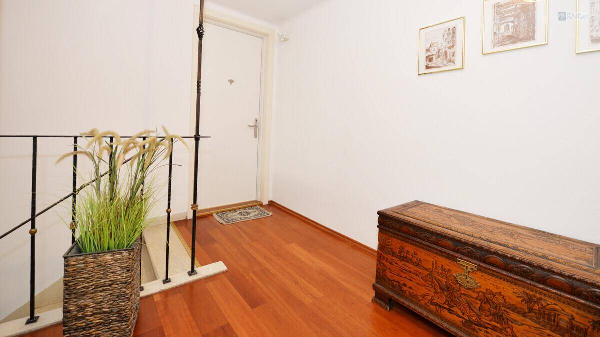 Heller Flur mit glänzendem Holzfußboden, einem dekorativen Holztruhe und Treppengeländer.